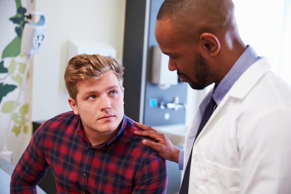 A doctor speaking with a patient in an exam room. 