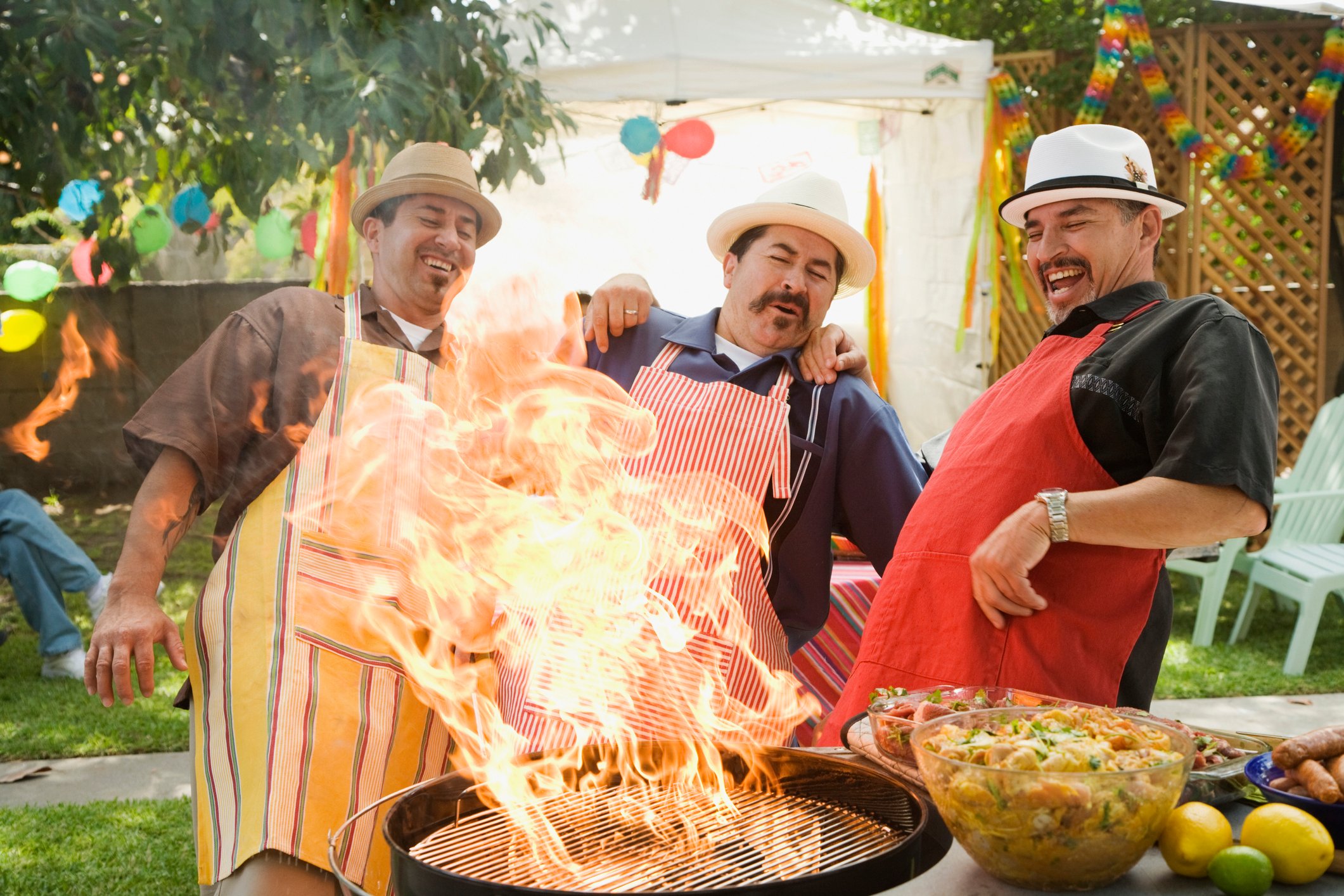 Three people around a grill with a huge flame.