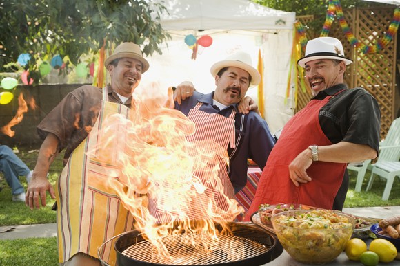 Three people around a grill with a huge flame.