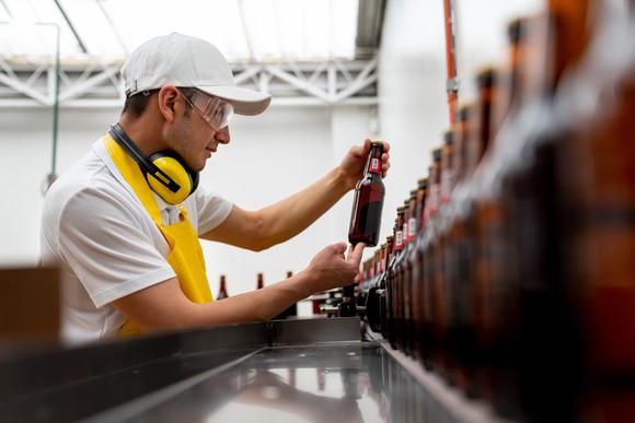 A worker inspecting a bottle on a beer bottling assembly line.