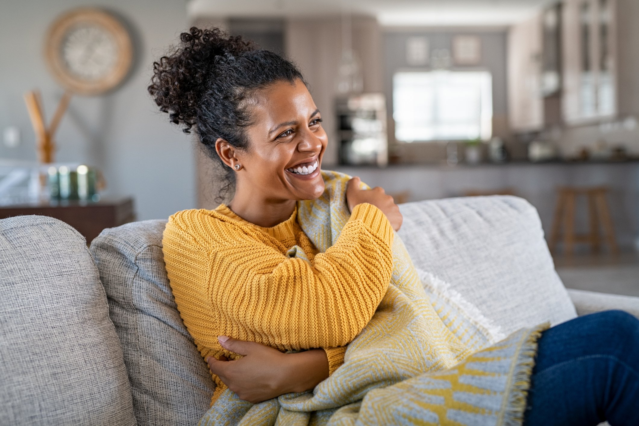 happy smiling woman sitting on living room couch wrapped in blanket