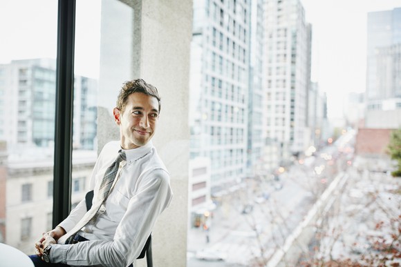 Happy businessperson looking out office window into city below.