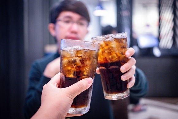 Two people raise their glasses filled with iced soda