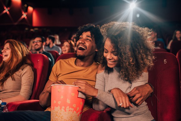 A couple in a theater laughing and eating popcorn.