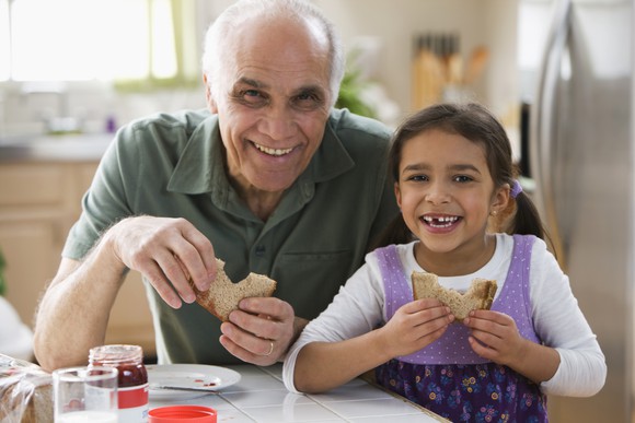 A smiling adult and child enjoying peanut butter and jelly sandwiches.
