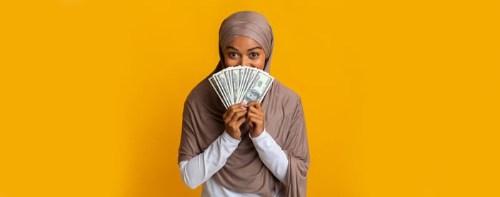 A person is holding fanned out money in front of half her face.