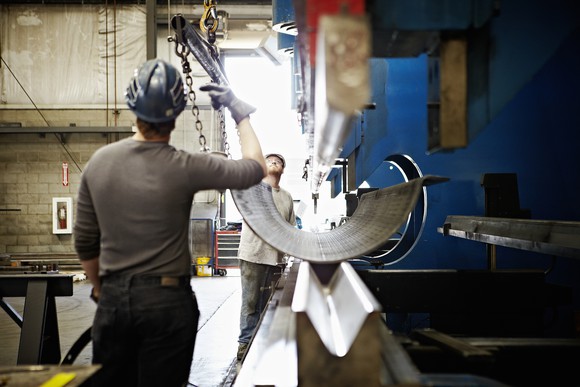 Two steelworkers in a factory working on a curved sheet of steel.