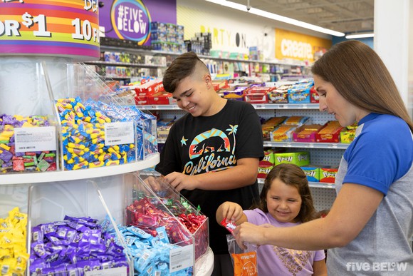 A Five Below employee helping a child shop for candy in a store.