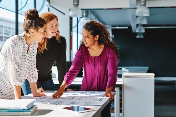 Three people looking at designs on a table.