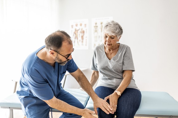 Physician is touching knee of patient sitting on exam table.