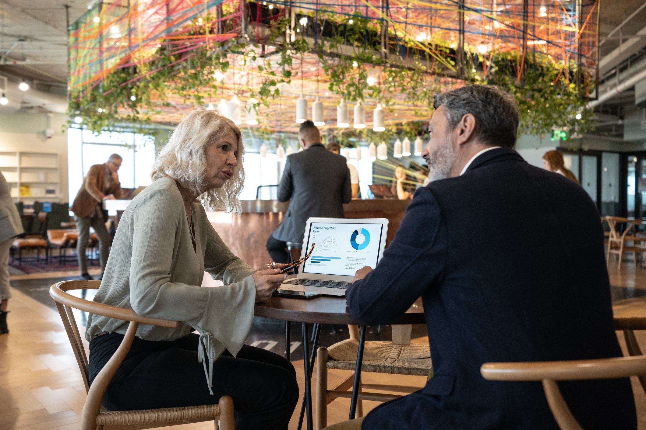 A couple sitting at a table talking while a laptop is in front of them.