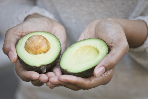 A woman holding a split avocado.