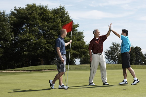 Three people on golf course. One is holding the flag and the other two are giving a high-five.