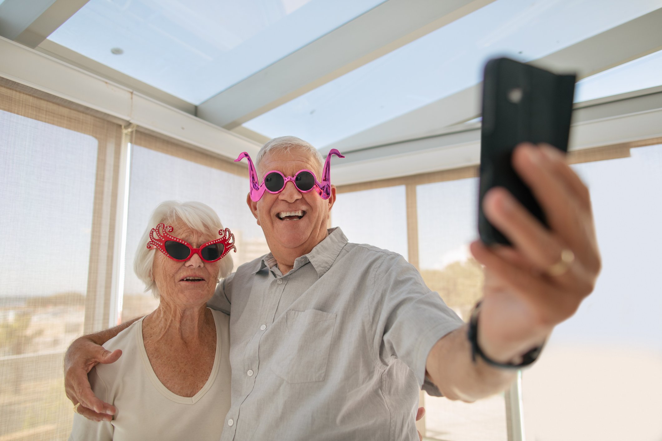 A older couple with silly glasses on taking a selfie at the beach.