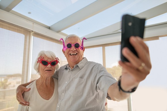 A older couple with silly glasses on taking a selfie at the beach.