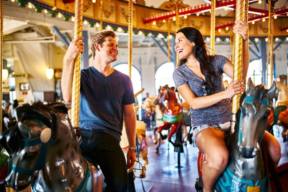 Two smiling people riding a carousel.