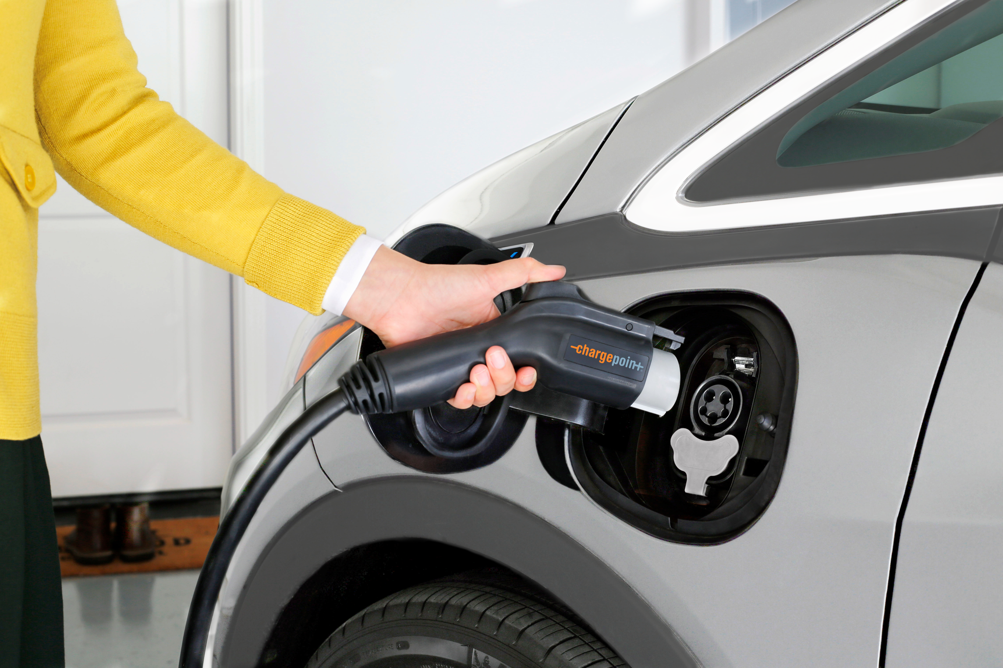 Electric vehicle owner plugging ChargePoint charger into car. 