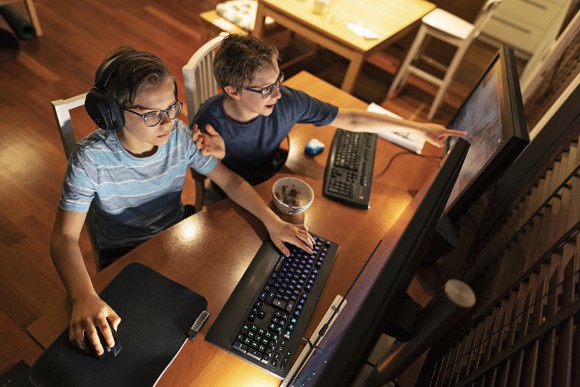 Two kids playing a video game on a personal computer.
