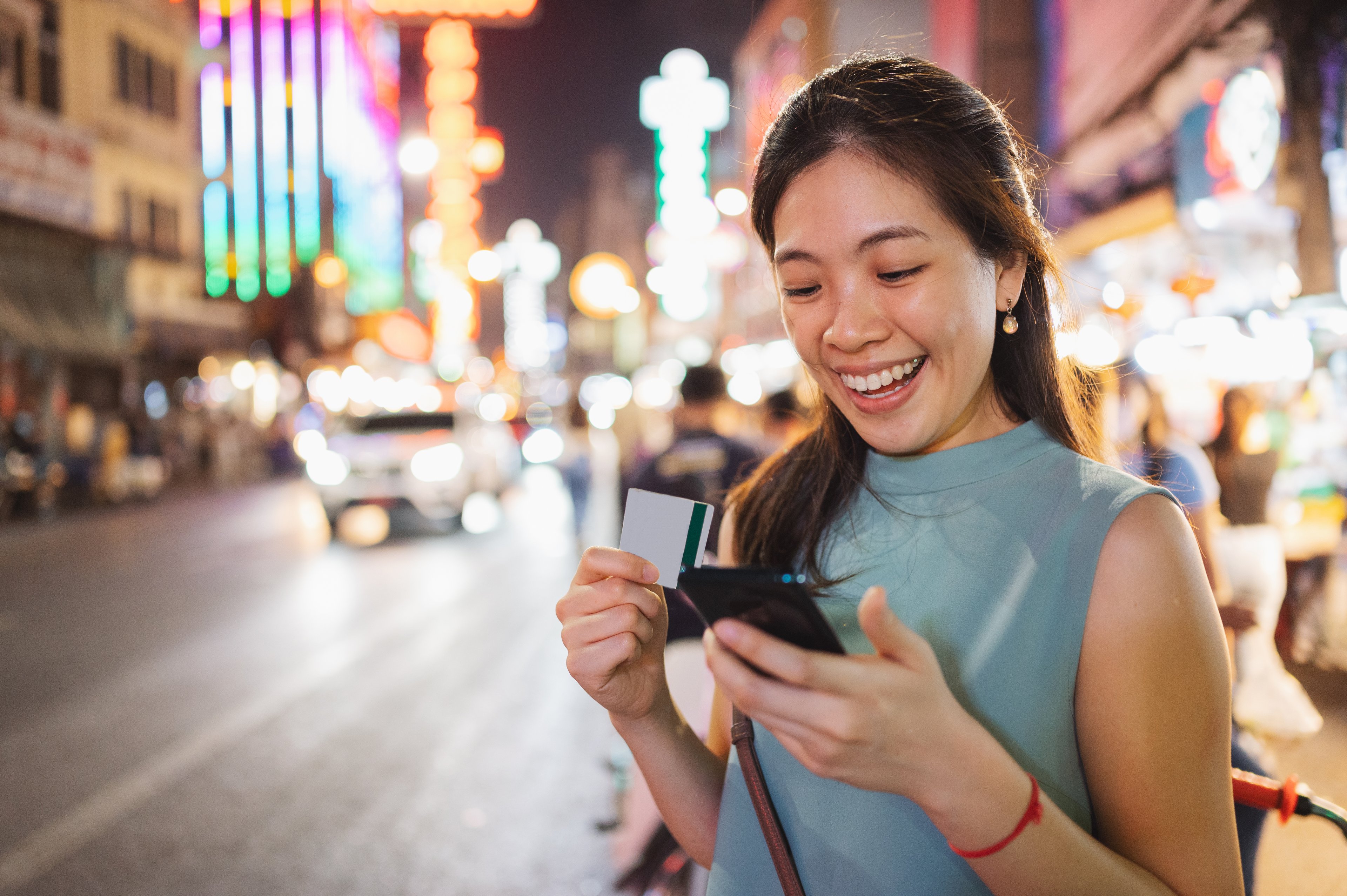 Person standing outside smiling with a credit card and cell phone in their hands.