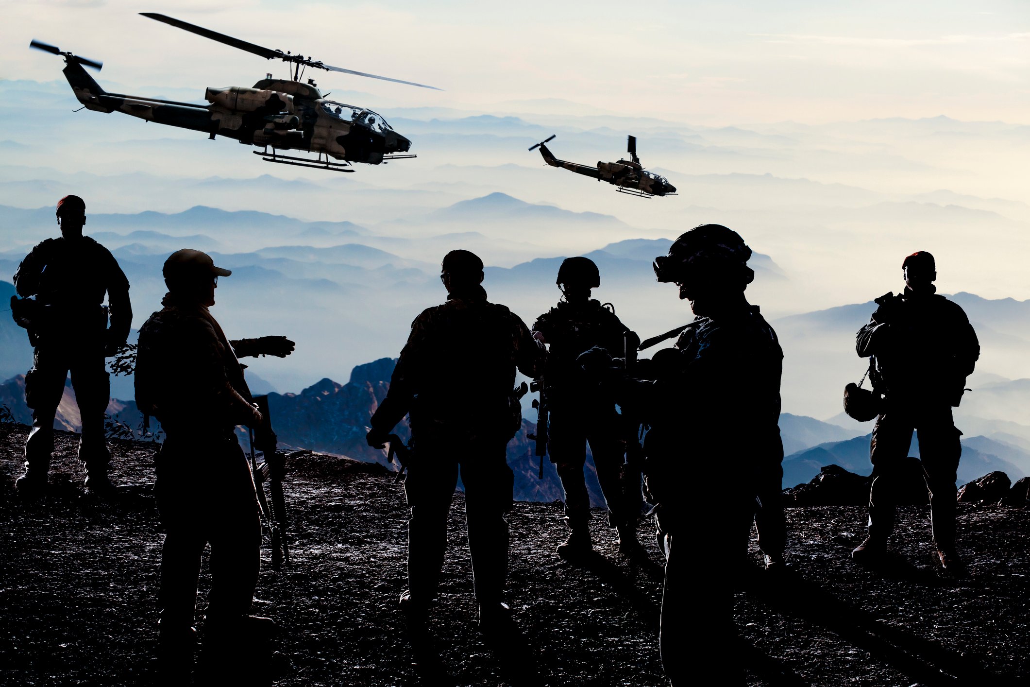 Six soldiers standing together during military training with two helicopters flying overhead.