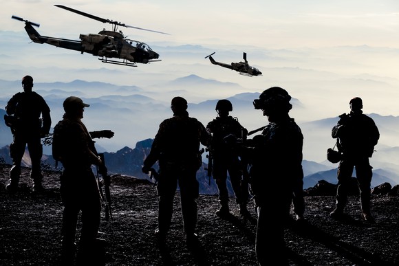 Six soldiers standing together during military training with two helicopters flying overhead.