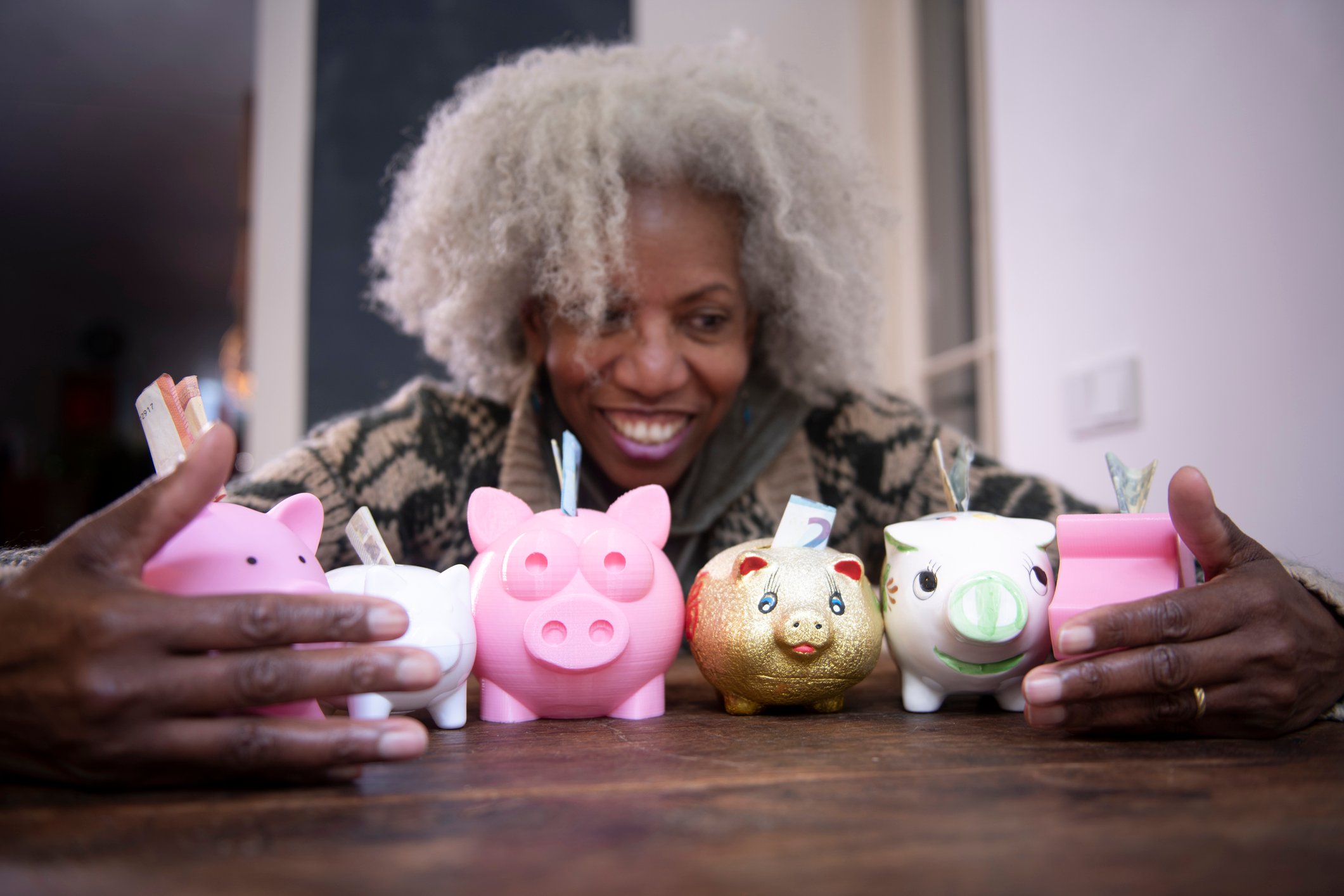 Older person with their hands surrounding six piggybanks with money coming out of each one of them.