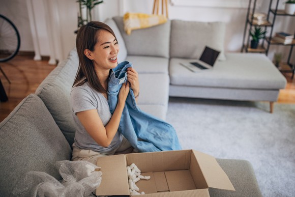 A customer holding a pair of jeans next to an open parcel box.