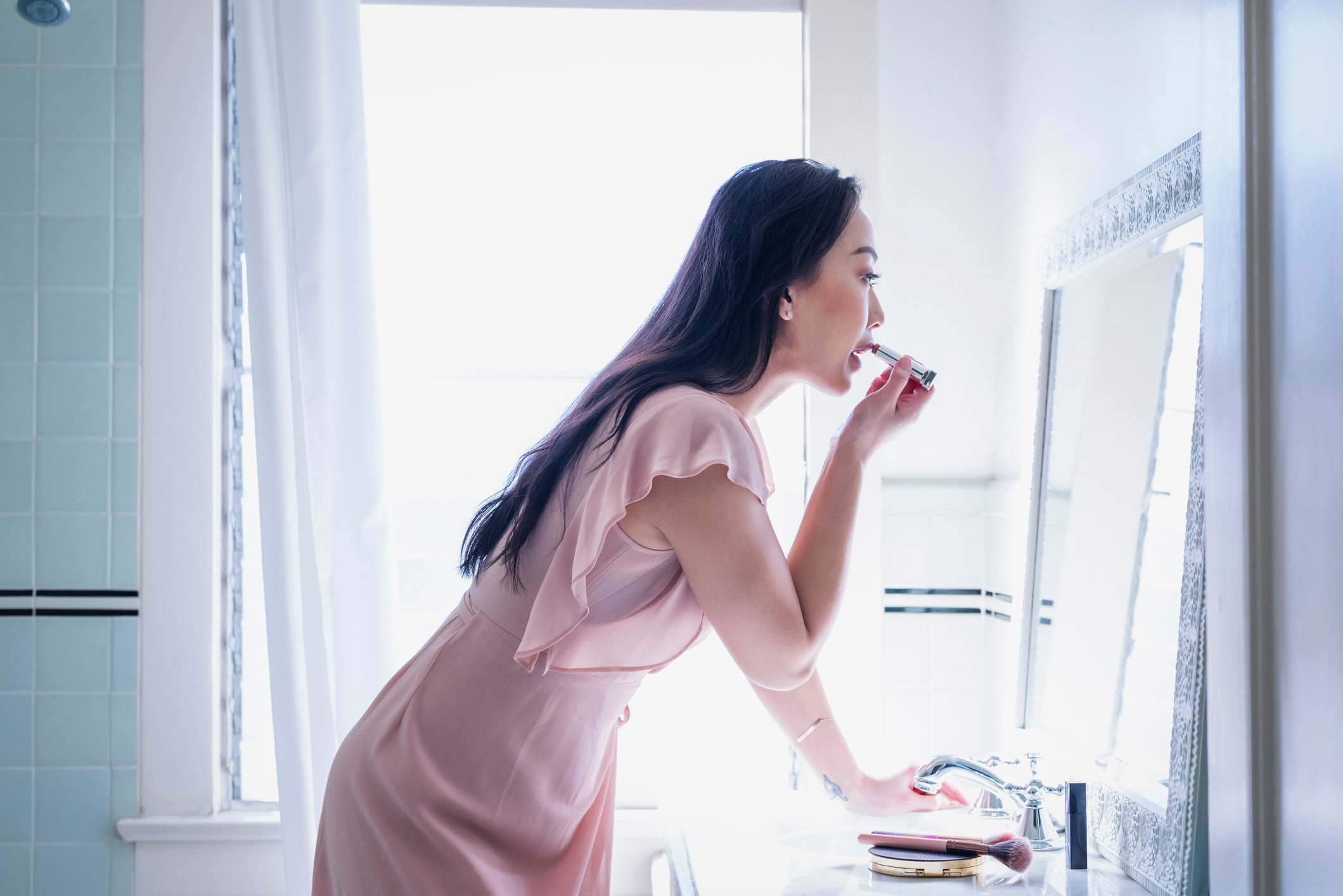 Woman applying lipstick in front of a mirror.