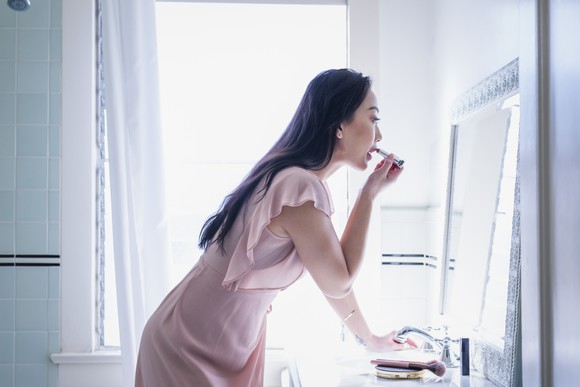Woman applying lipstick in front of a mirror.