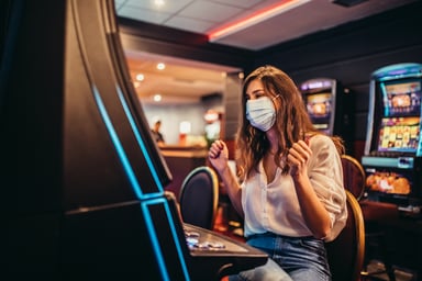 A masked woman plays a slot machine at a casino