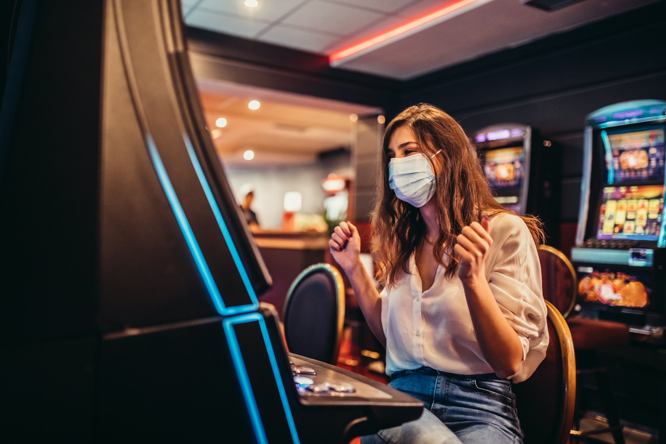 A masked customer plays a slot machine at a casino.