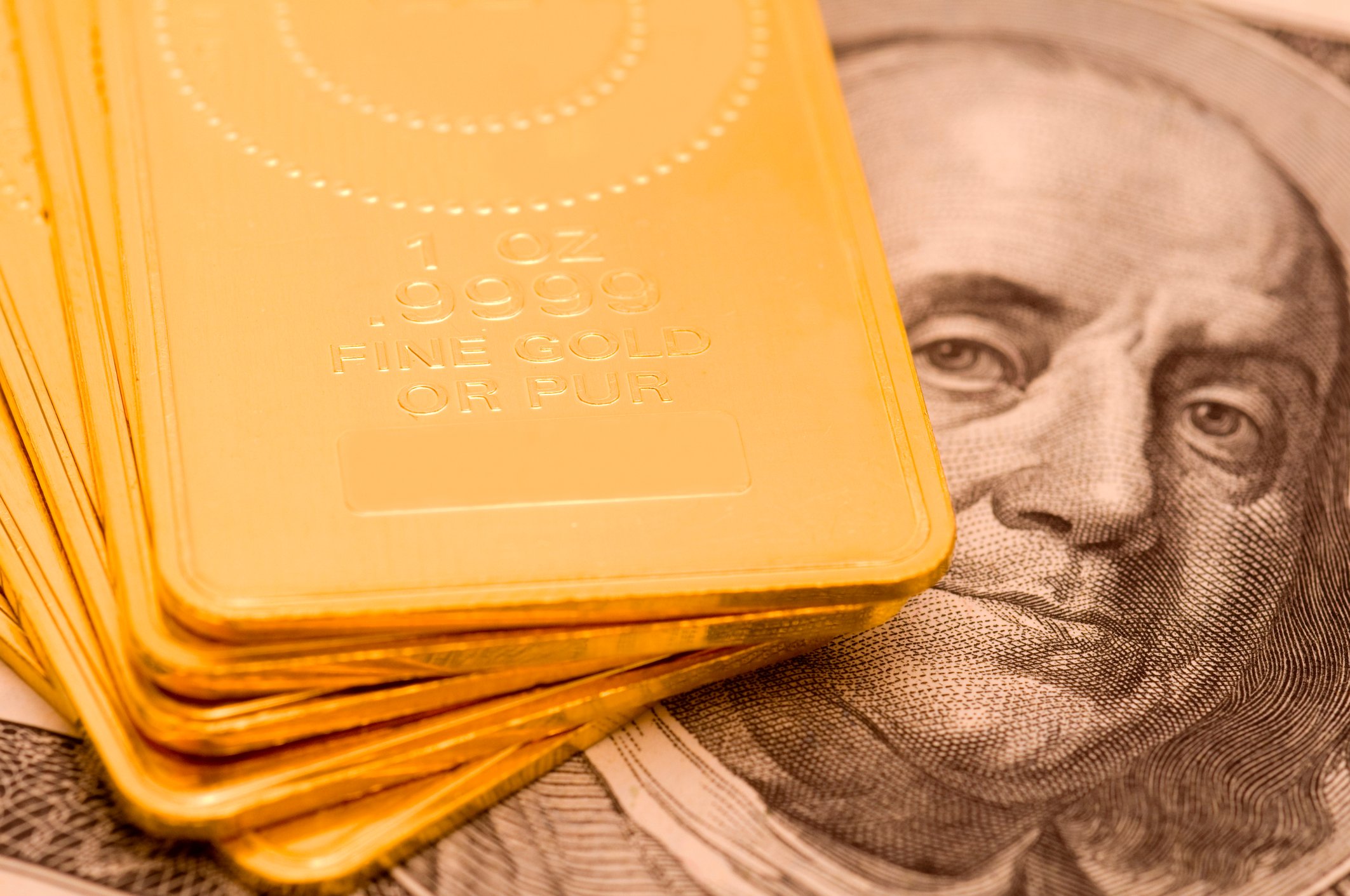 A staggered stack of gold ingots set atop a one hundred dollar bill.