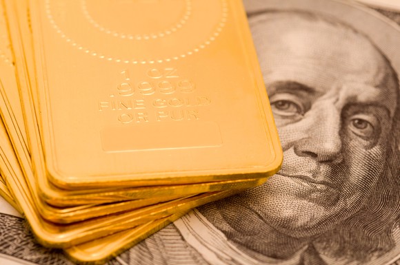 A staggered stack of gold ingots set atop a one hundred dollar bill.
