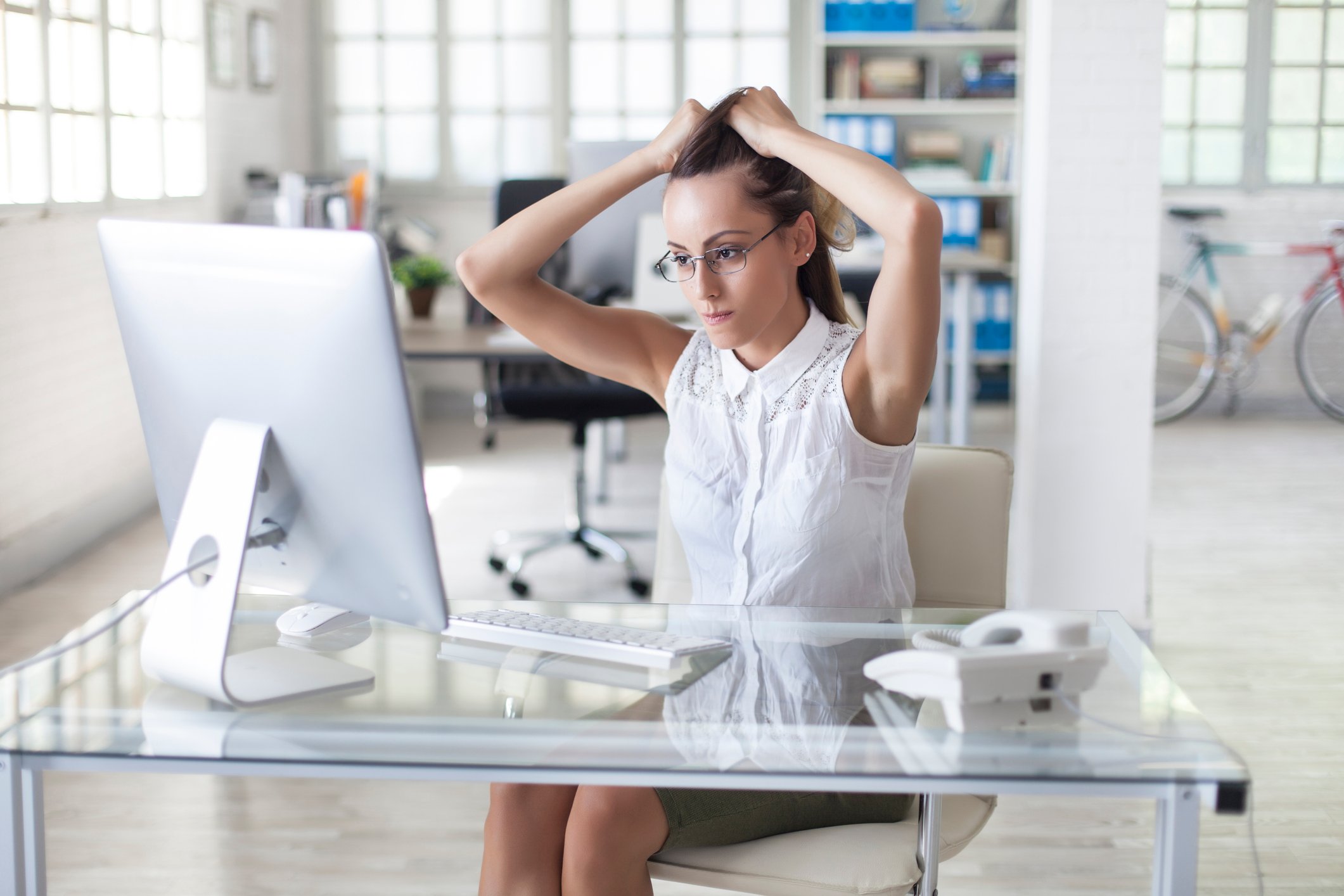 Person holding hair looking at computer screen.