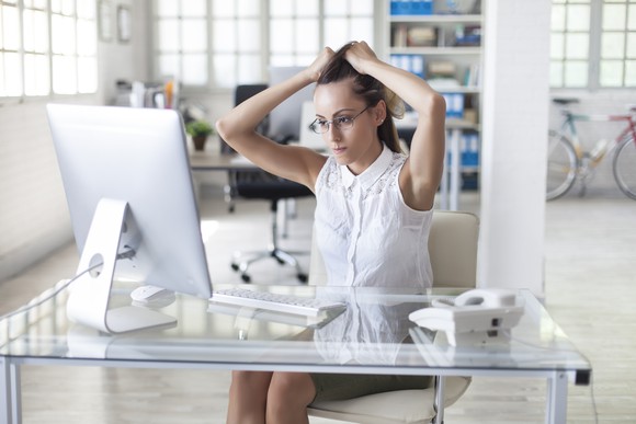 Person holding hair looking at computer screen.