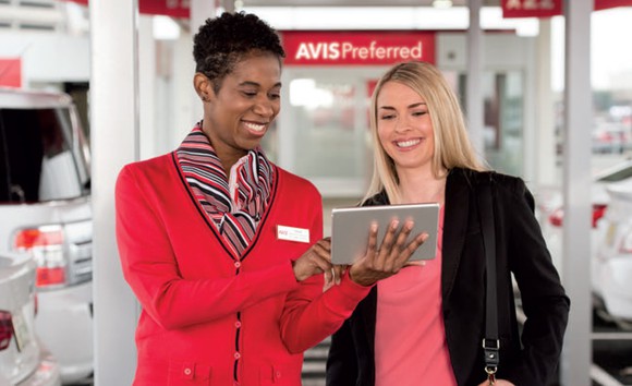 Two people looking at a tablet, with Avis signage and uniform.