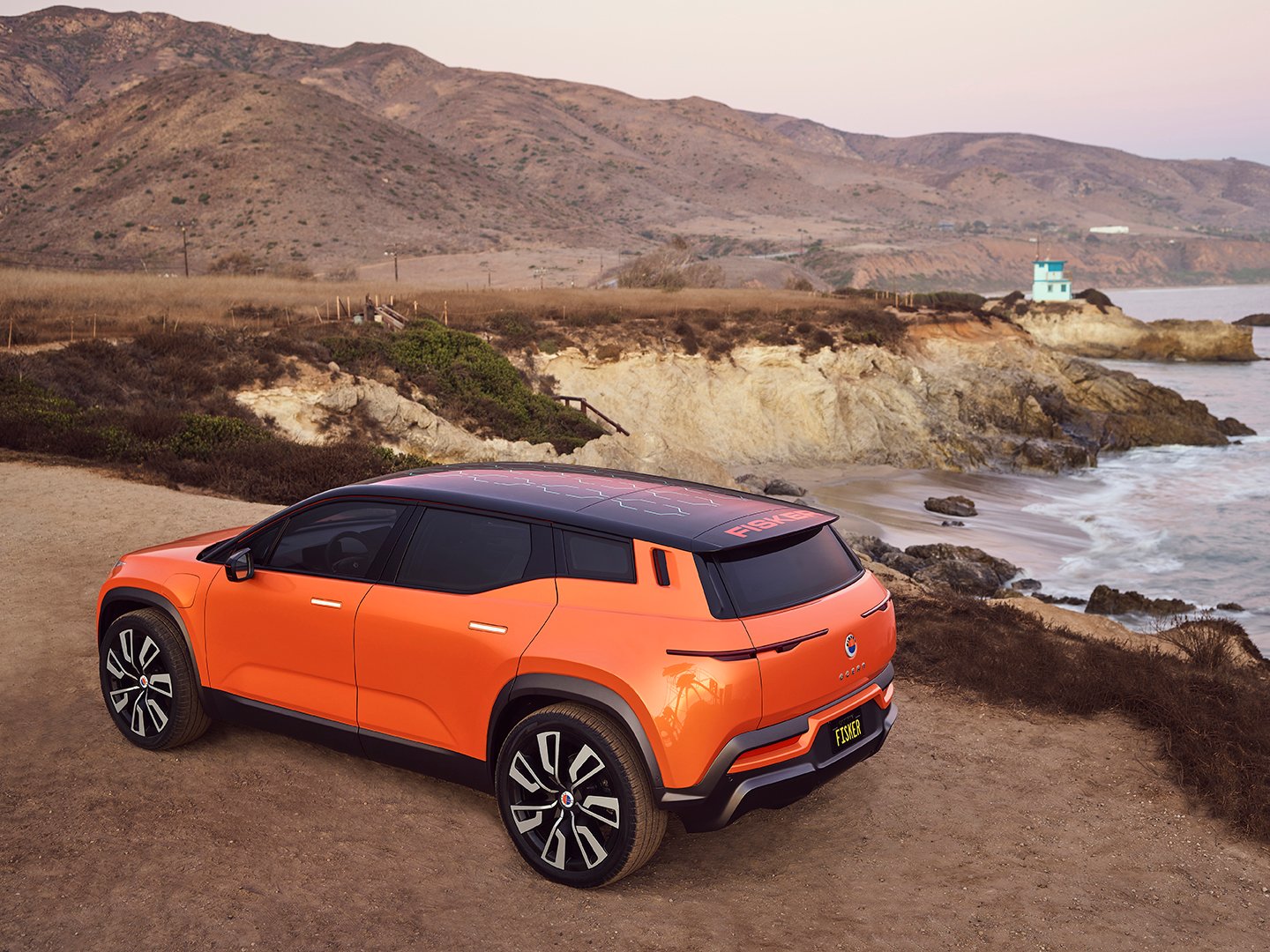 An orange Fisker Ocean prototype shown parked by the ocean.