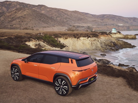 An orange Fisker Ocean prototype shown parked by the ocean.