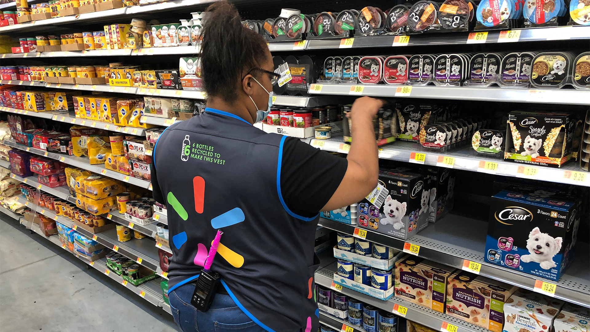 A Walmart employee stands in an aisle and reaches for an item on the shelf of a store