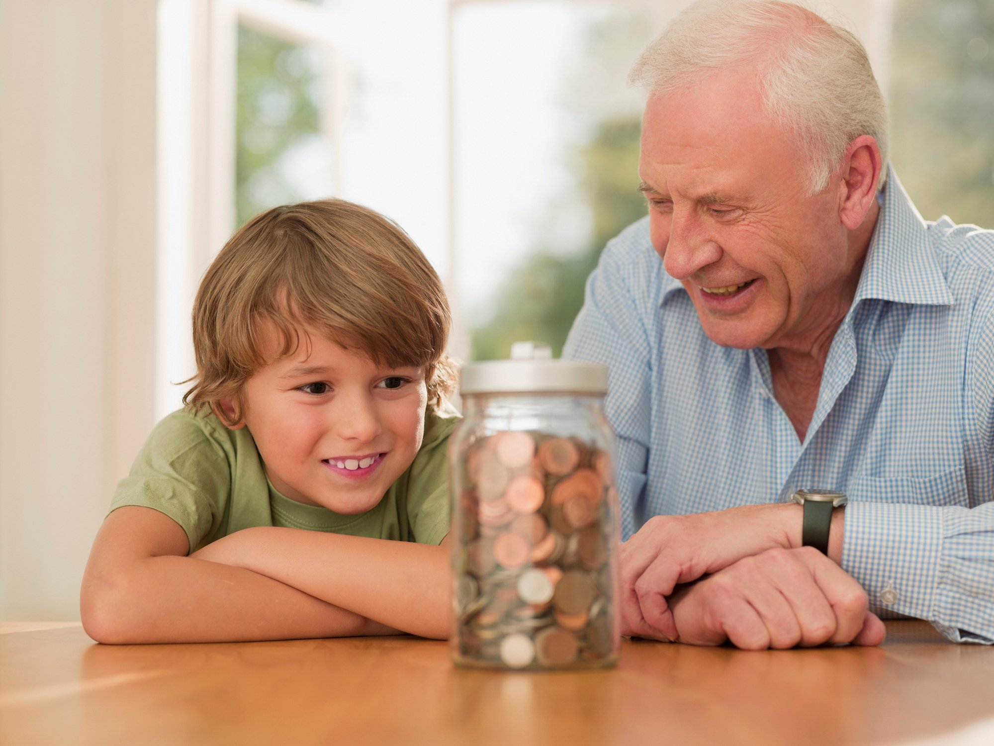 Smiling young child and smiling senior citizen look at a jar full of coins. 