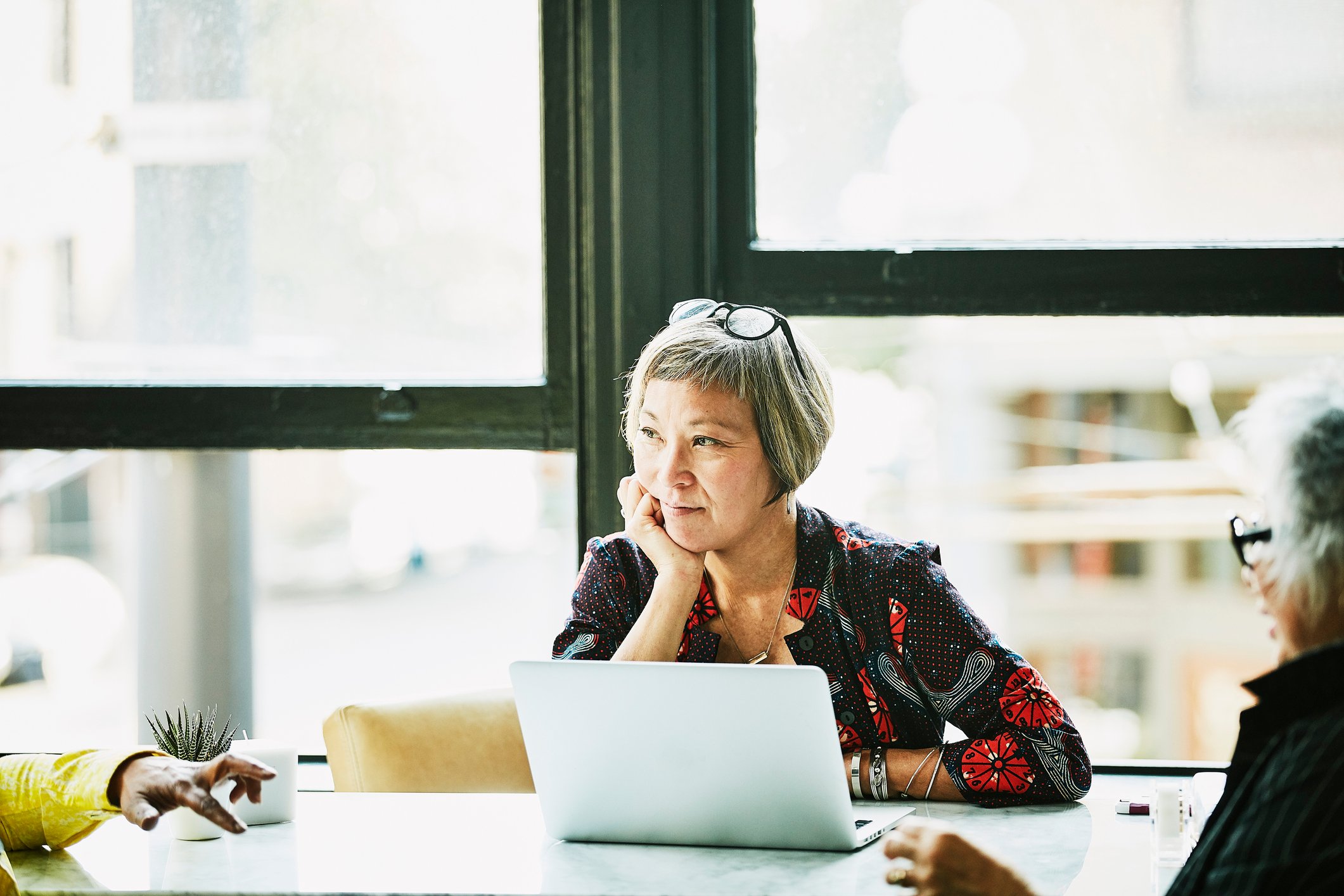 A woman in an office setting sits pensively at a laptop,