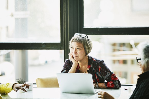 A woman in an office setting sits pensively at a laptop,