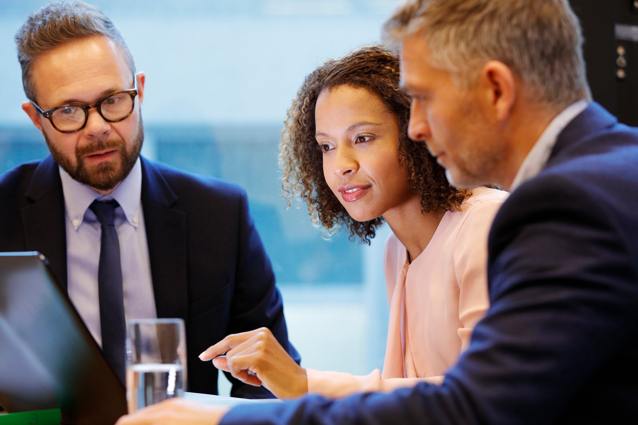 Three people in business attire are gathered around a laptop screen.