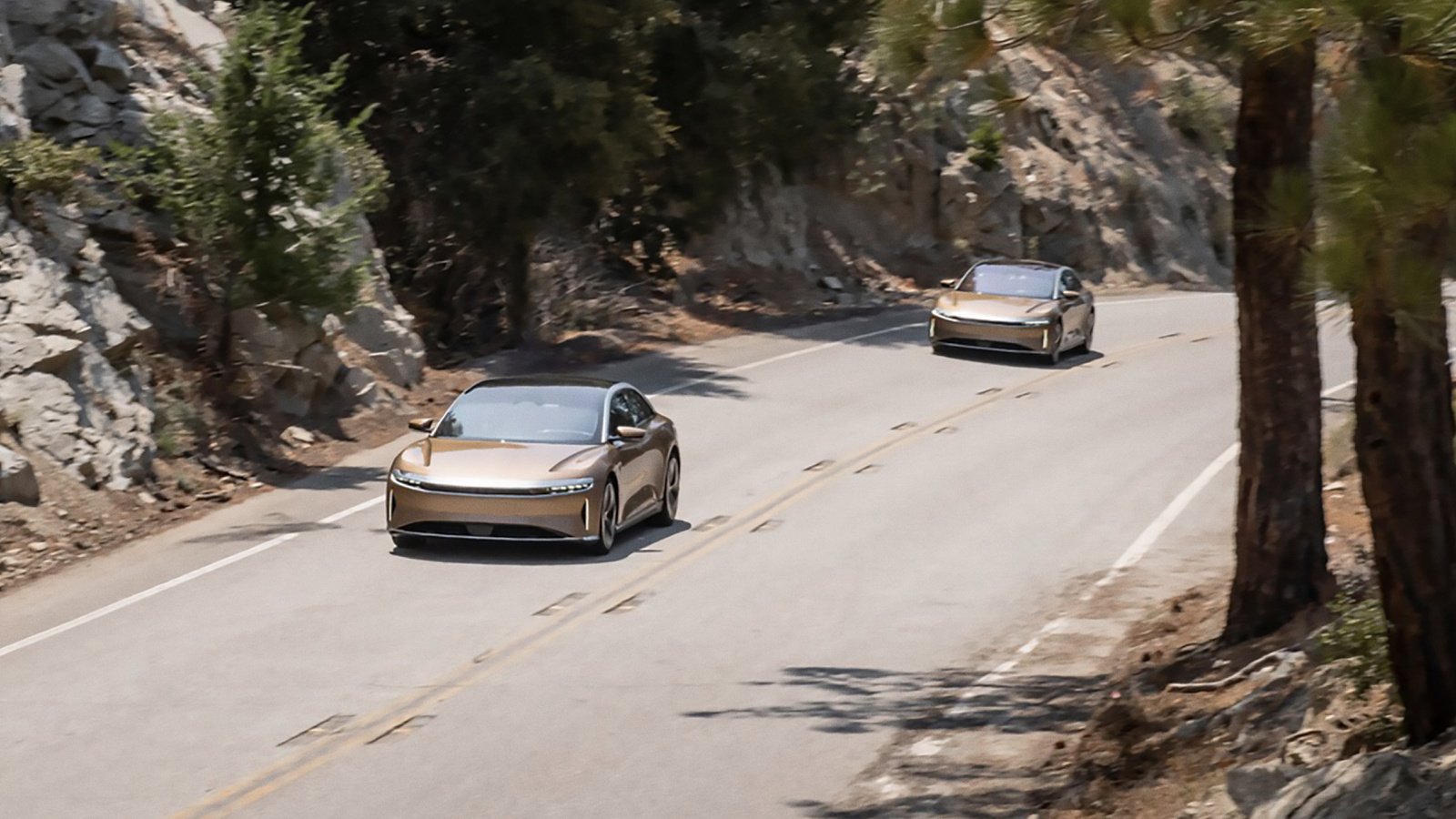 Two gold Lucid Air luxury electric sedans on a mountain highway.