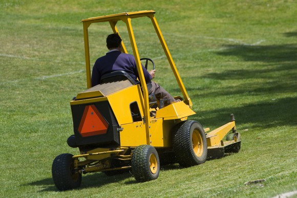 An industrial riding lawnmower being used to cut a lawn.