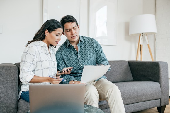 Two people sitting on a couch looking at documents.