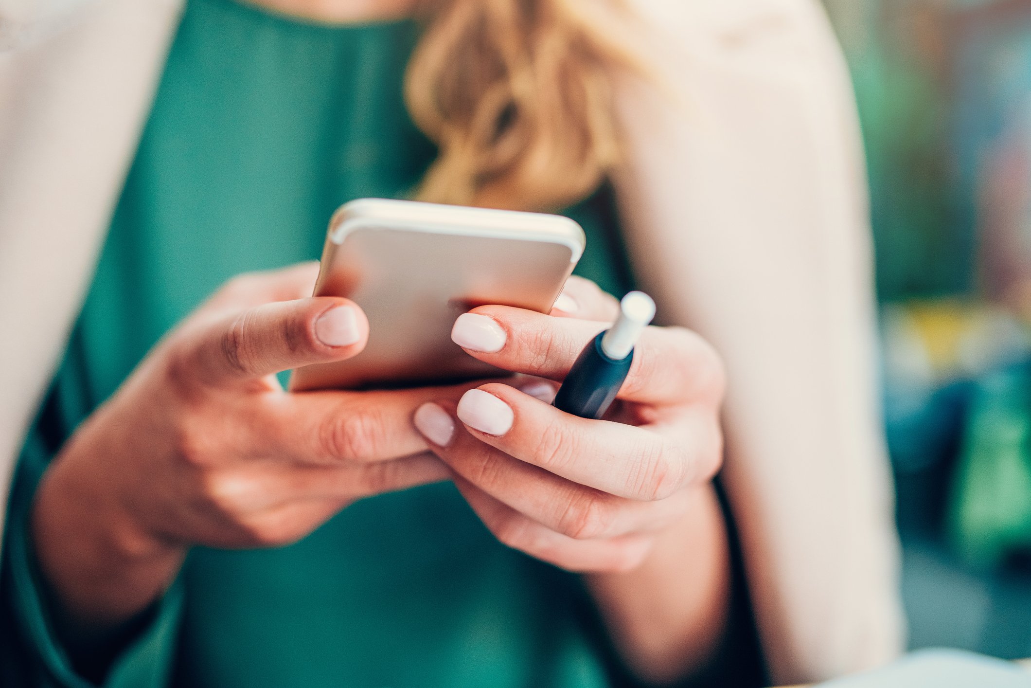 A person holding a smartphone and an e-cigarette.