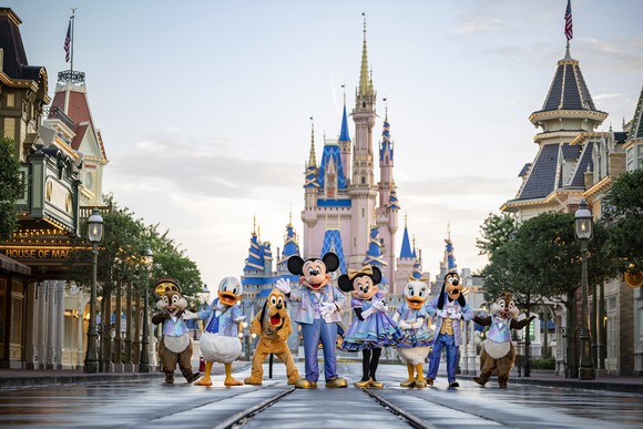 Mickey Mouse and his friends dressed in outfits celebrating 50 years in front of the Magic Kingdom castle in Disney World.