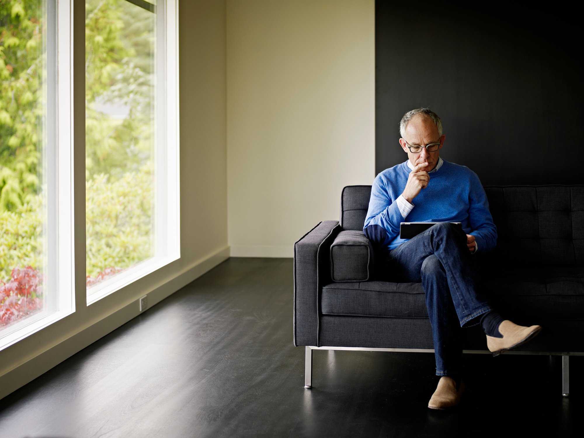 older man sitting on a chair and looking at a tablet.