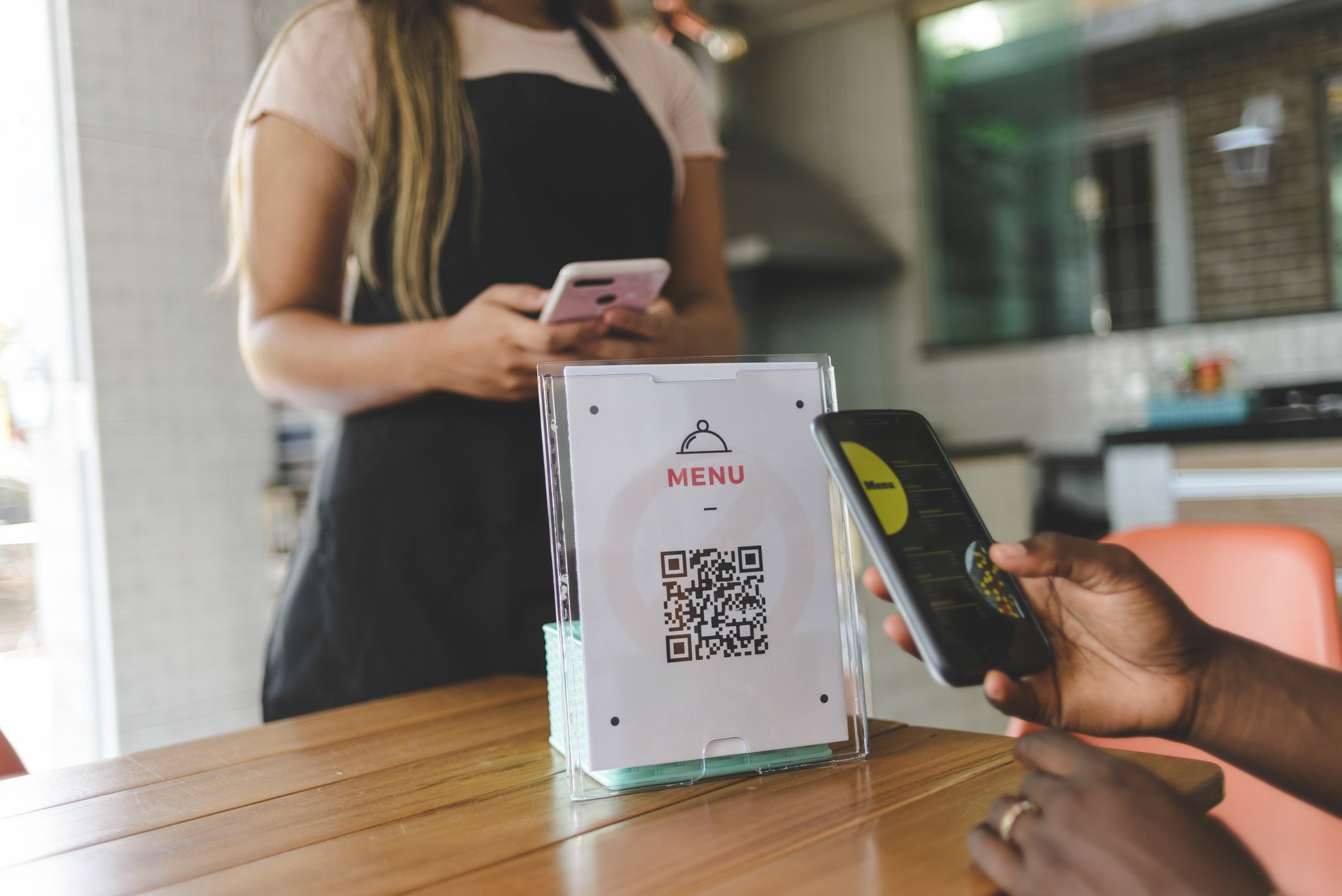 Two people with cell phones use a QR code to pull up a menu. 